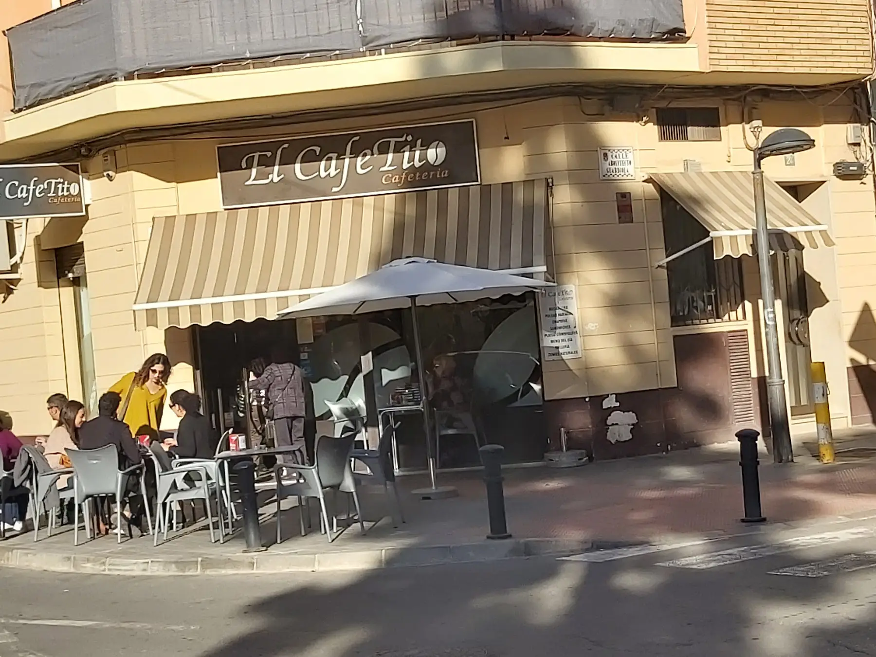 La esquina de El Cafetito: el rótulo, el toldo a rayas y la terraza al sol con clientes